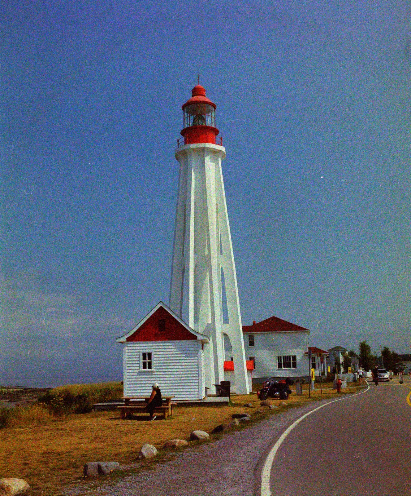 A red and white lighthouse beside a white house and a curved road, converted with Fine 50