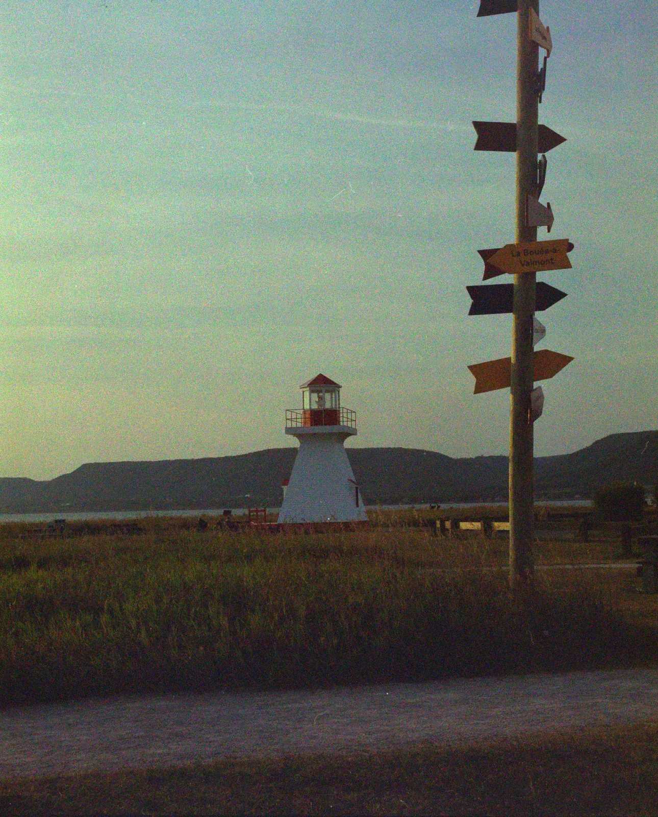 A signpost and a small lighthouse by the water, converted with Interpositive